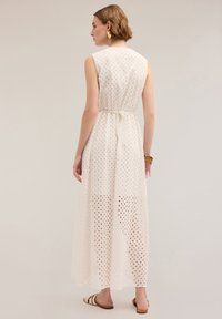 Rochie maxi albă, cu un model de ochi perforat, talie cu curea, fără mâneci și o siluetă fluidă.