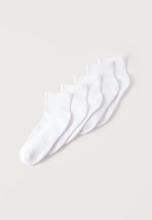 Cinq chaussettes blanches de cheville disposées en éventail sur un fond clair.