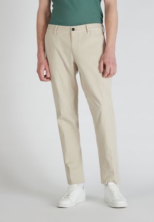 Beige Chinos mit geradem Schnitt, aus weichem Baumwollstoff. Ausgestattet mit einem einzelnen schwarzen Knopf und Seitentaschen, kombiniert mit weißen Sneakern.