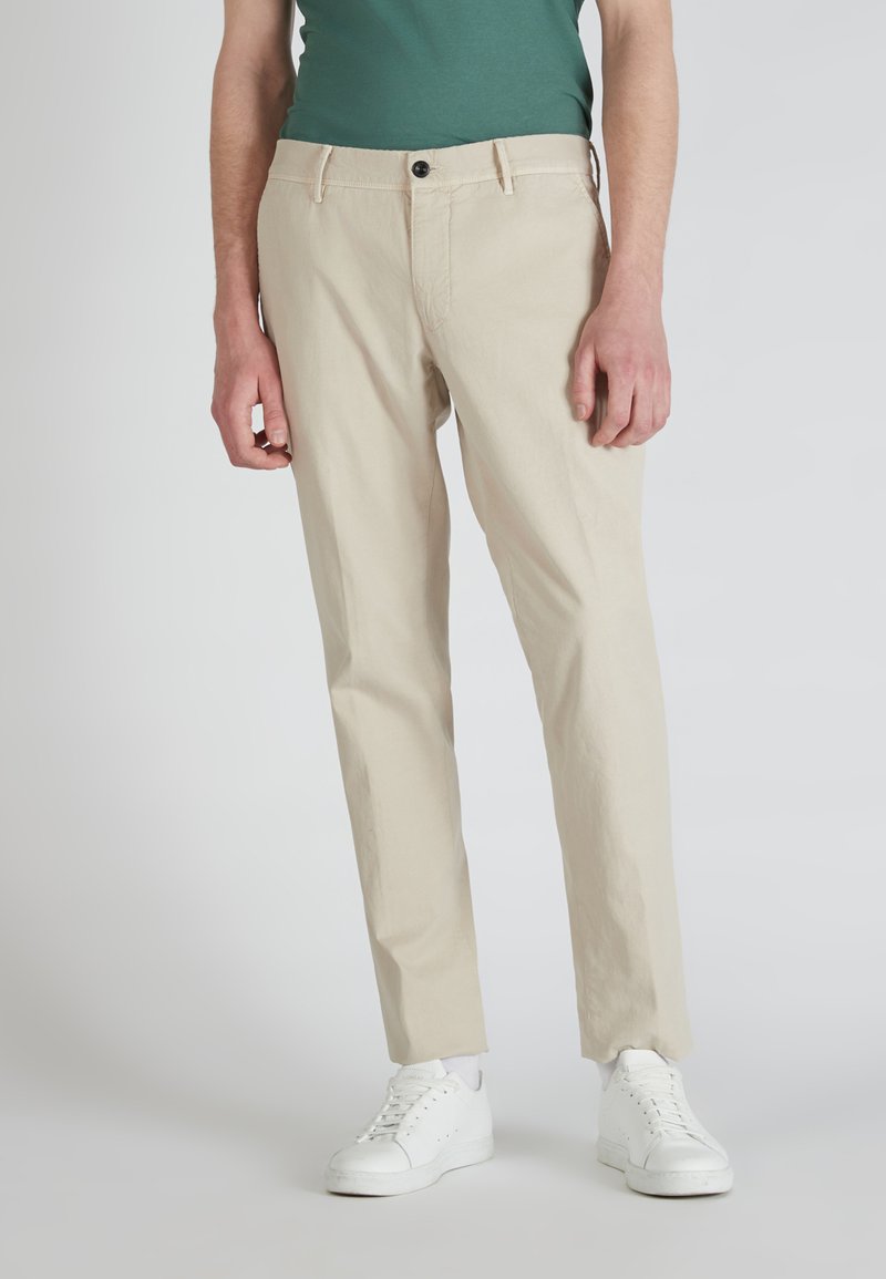 Beige chino's met een rechte pasvorm, gemaakt van zachte katoenen stof. Voorzien van een enkele zwarte knop en zijzakken, gecombineerd met witte sneakers.