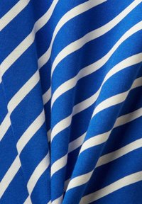Tissu bleu avec des rayures diagonales blanches uniformément espacées formant un motif ondulé avec une texture et des plis visibles.
