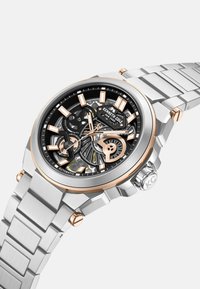 Srebrny zegarek ze stali nierdzewnej z czarną i złotą szkieletem tarczą, różowozłotymi akcentami oraz solidnym bransoletem. Posiada mechanizm automatyczny.