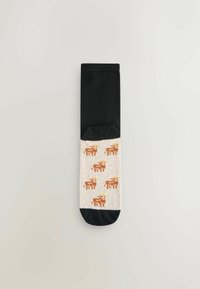 Zwarte en crèmekleurige katoenen sokken met een patroon van oranje-bruine grasetende koeien op het crèmekleurige gedeelte, met een stevig zwarte bovenkant en teen.