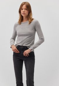 Graues langärmliges Oberteil aus strukturiertem Strickstoff, mit Rundhalsausschnitt und goldfarbenen Knopf-Akzenten an den Ärmelbündchen, kombiniert mit schwarzen Jeans.