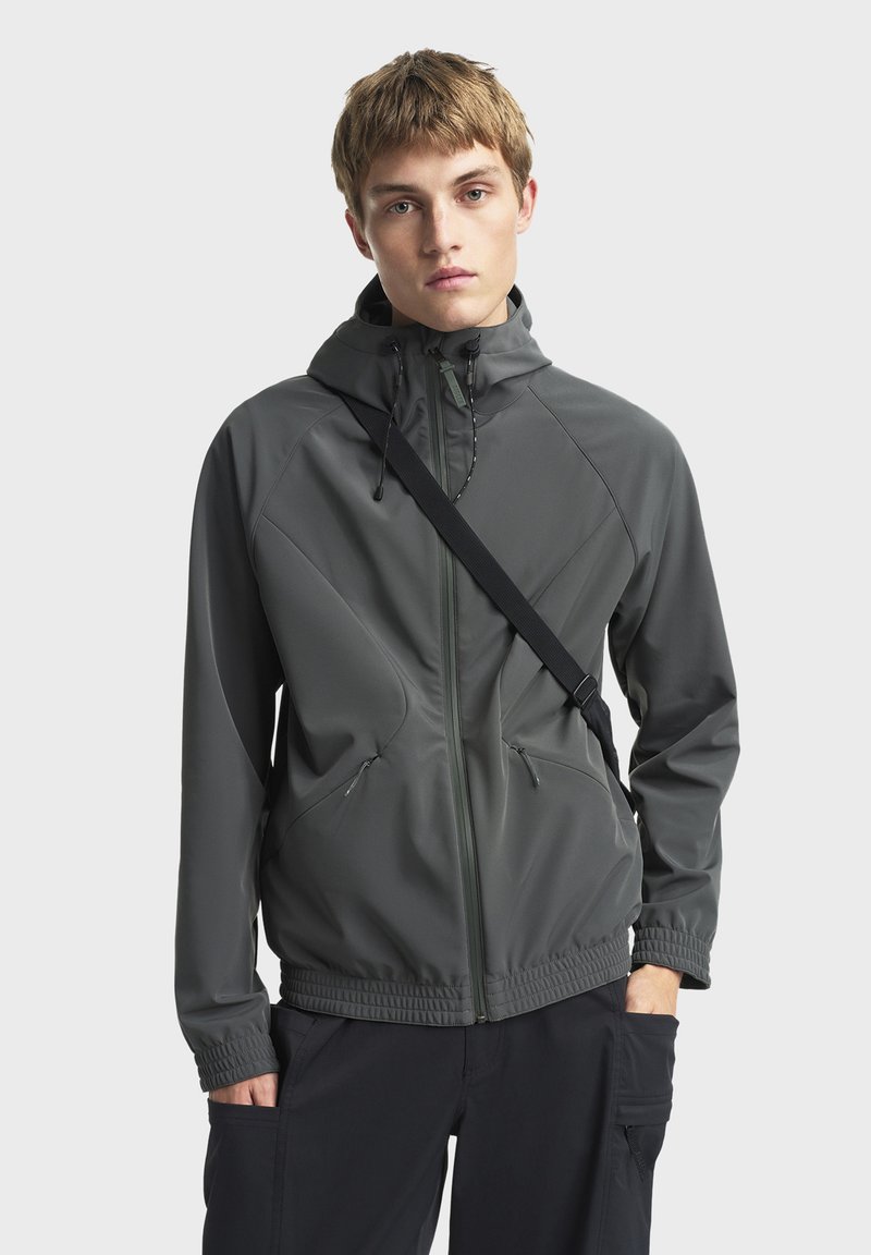 Grå, letvægtsjakke med hætte, lynlåslukning foran og elastiske manchetter. Har vinklede sømdetaljer og sidelommer.