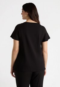 Top scurt negru cu mânecă scurtă și croială lejeră, având un decolteu rotund și o textură fină. Vederea din spate arată șlițuri subtile pe laterale la margine.