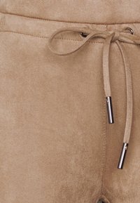 Shorts en suède beige avec une taille à cordon de serrage. Présente des embouts métalliques sur le cordon et une surface douce et texturée.