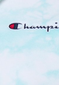 Bavlněné tričko s jemným modrým tie-dye vzorem, se strašně vyšitým logem "Champion" v černé a červené barvě na hrudi.