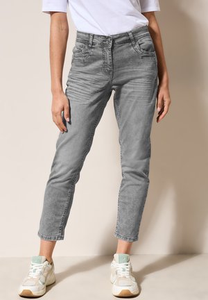 Jeans de denim gris con un corte ajustado, que presentan bolsillos laterales, una cintura alta y una textura ligeramente desgastada. Combinados con zapatillas de color claro.