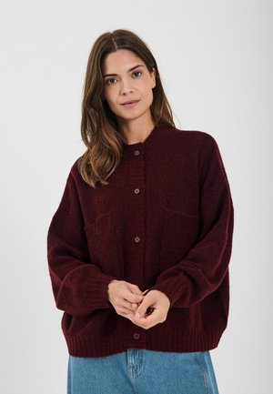 Cardigan in magenta a maglia con grandi bottoni e due tasche anteriori. Presenta una vestibilità rilassata e dettagli a coste su polsini e orlo.