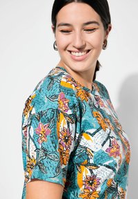 Korte mouw shirt in teal met een levendig bloemmotief in oranje en roze. Katoenen stof met een relaxte pasvorm en ronde hals.