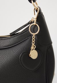 Black textured faux leather handbag with a gold-tone zipper and hardware. Features a heart-shaped accent and a decorative charm.