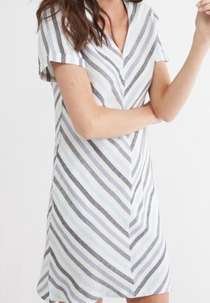 Femme portant une robe à manches courtes et col en V avec des rayures diagonales grises, noires, bleu clair et blanches sur un fond clair.