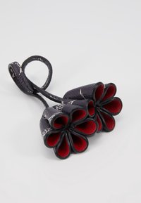 Černý a červený květinový přívěsek vyrobený z texturovaného materiálu, který obsahuje dva květinové tvary s vrstvenými okvětními lístky a očko pro připevnění.