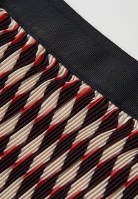 Tessuto a pieghe con un motivo geometrico nei colori crema, rosso e nero. Presenta una cintura nera texturizzata e rigata. Finitura liscia complessiva.