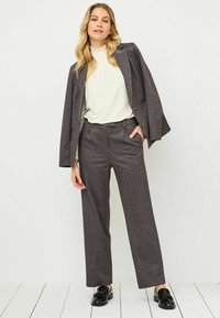 Grijze, gestructureerde blazer met bijpassende high-waisted broek; witte geplooide blouse eronder; zwarte schoenen. Soepele stof en rechte snit.