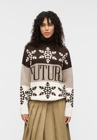 Pull à col roulé marron et crème avec des motifs de flocons de neige et le mot "FUTURE" en caractères gras, doté de poignets et d'un ourlet côtelés.