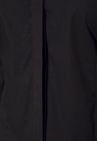 Camicia nera con bottone, caratterizzata da un design semplice, linee pulite e un tessuto liscio e texture. Nessun motivo visibile o accenti aggiuntivi.