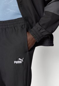 Schwarze Sporthosen mit elastischem Bund, Logodruck und glatter Textur, kombiniert mit einer passenden Jacke mit grauen Akzenten.
