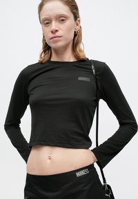 Mustan pikkuseeliku puudel, mis on valmistatud pehmest kangast ja millel on kehasse sobiv disain. Esiosas on väike logo ja tekstuuriga varrukad.