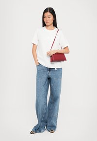 White t-shirt with embroidered design, paired with wide-leg blue jeans. A small red leather handbag with a shoulder strap is worn.