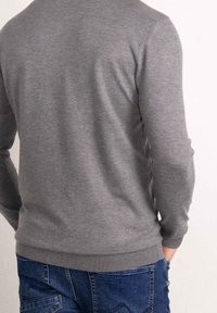 Pull en maille grise à manches longues, col rond, poignets et ourlet côtelés, vu de dos, assorti à un jean bleu.