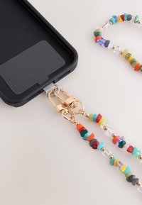 Coque de téléphone noire avec une chaîne en perles colorées et des éléments en métal doré, équipée d'un connecteur en plastique pour fixation.