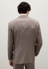 Giacca di suit marrone chiaro con finitura testurizzata, rever a punta e maniche con tre bottoni. Vestibilità su misura con leggero imbottitura sulle spalle e retro ventilato.