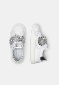 Vita sneakers i slätt läder, med silverfärgade blommotiv och svarta accenter. Gummisula och kardborreband som stängning.