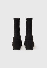 Black suede ankle boots with a chunky heel, featuring a zip closure at the back. Smooth texture and minimalist design.