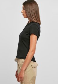 Svart kortermet topp med ribbet tekstur, bølgende kanter og en tett passform, parret med beige cargo-bukser med sidelommer.