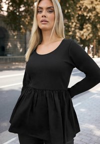 Musta paita pitkähihaisilla, ylhäällä rypytetty pinta ja levenevä, kerätty alaosa. Pyöreä kaula-aukko ja minimaalinen muotoilu.