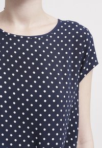 Navyblaues kurzärmliges Shirt mit weißen Polka-Dots, rundem Ausschnitt, weichem Stoff und lockerer Passform ohne sichtbare Akzente.