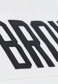 Nahaufnahme von schwarz gestickten Buchstaben auf weißem Stoff, die detaillierte Stickerei und Textur zeigen.