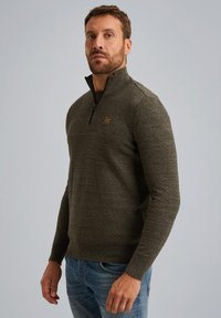Olijfgroene zip-neck trui, met een gestructureerde stof, slim fit, voorzien van een klein logo op de borst. G gedragen met lichtblauwe jeans.