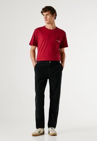 Rode katoenen T-shirt met korte mouwen en een borstzak, gecombineerd met zwarte corduroypantalons en gepatternde sneakers. Eenvoudige en casual outfit.