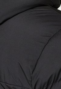 Gros plan sur un tissu matelassé noir avec des coutures visibles et de légers plis, suggérant une veste ou un manteau chaud.