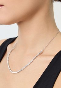 Kobieta nosząca srebrny naszyjnik z małymi, okrągłymi, równomiernie rozmieszczonymi kamieniami szlachetnymi, w zestawieniu z czarnym topem bez rękawów.