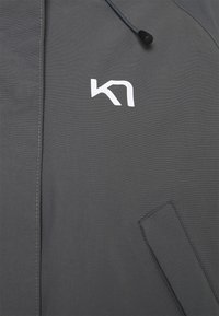 Szara kurtka charakteryzuje się gładką teksturą, z białym logo i kontrastowym przeszyciem. Wartością dodaną są sznurki regulacyjne oraz boczna kieszeń.