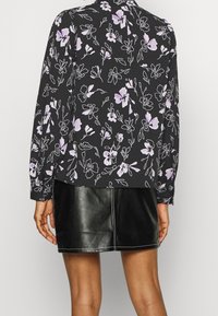 Blusa nera floreale con motivi di fiori viola e bianchi, maniche lunghe e una vestibilità rilassata, abbinata a una mini gonna di pelle nera.