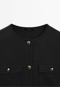 Cardigan en tricot noir avec encolure ronde, deux poches avant et boutons dorés décoratifs au centre et sur les rabats des poches.
