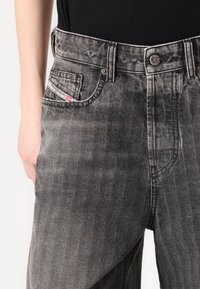 Grå denim jeans med et subtilt stripemønster, fem lommer og et merketikett på venstre frontlomme. Standard passform med knappelukking.