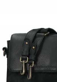 Zwarte leren tas met een korrelige textuur, gebogen vorm, voorzien van twee bronzen hardwareclips en een geperst logo op de voorkant.