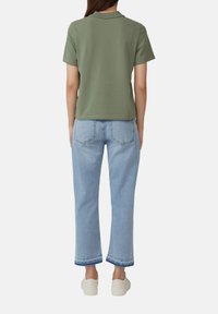 Oliwkowa koszulka polo z krótkim rękawem w połączeniu z jasnoniebieskimi, ściąganymi dżinsami o widocznych szwach i prostym kroju. Białe sneakersy.
