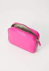 Pink leather cosmetic case with textured exterior, rectangular shape, top zipper, and subtle brand lettering on the front.