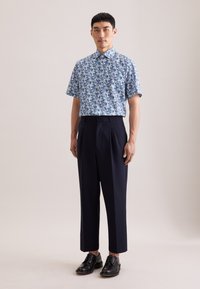 Korte mouwen blauw bloemenoverhemd gecombineerd met donkerblauwe, hoog getailleerde broek en zwarte nette schoenen. Glad materiaal, getailleerde pasvorm.