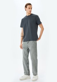 Camiseta de cuello redondo gris oscuro en suave algodón, combinada con jeans gris claro, que presentan un corte relajado y pierna recta, completada con zapatillas blancas.