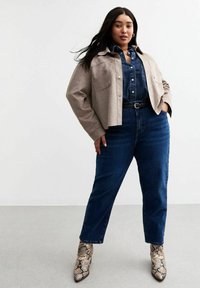 Chaqueta corta beige sobre una camisa de mezclilla, combinada con jeans oscuros de talle alto y botas de tobillo con estampado de serpiente.