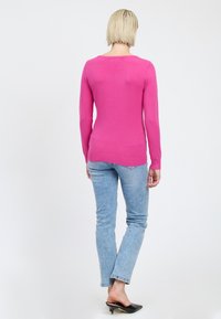 Maglione rosa a maniche lunghe con collo rotondo, vestibilità slim e fondo a coste, abbinato a jeans azzurri chiari e mule nere con tacco.