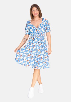 Vestido floral en azul, blanco y naranja; mangas cortas abullonadas; cintura ajustada con detalle de lazada; tela ligera; hasta la rodilla. Zapatillas blancas.